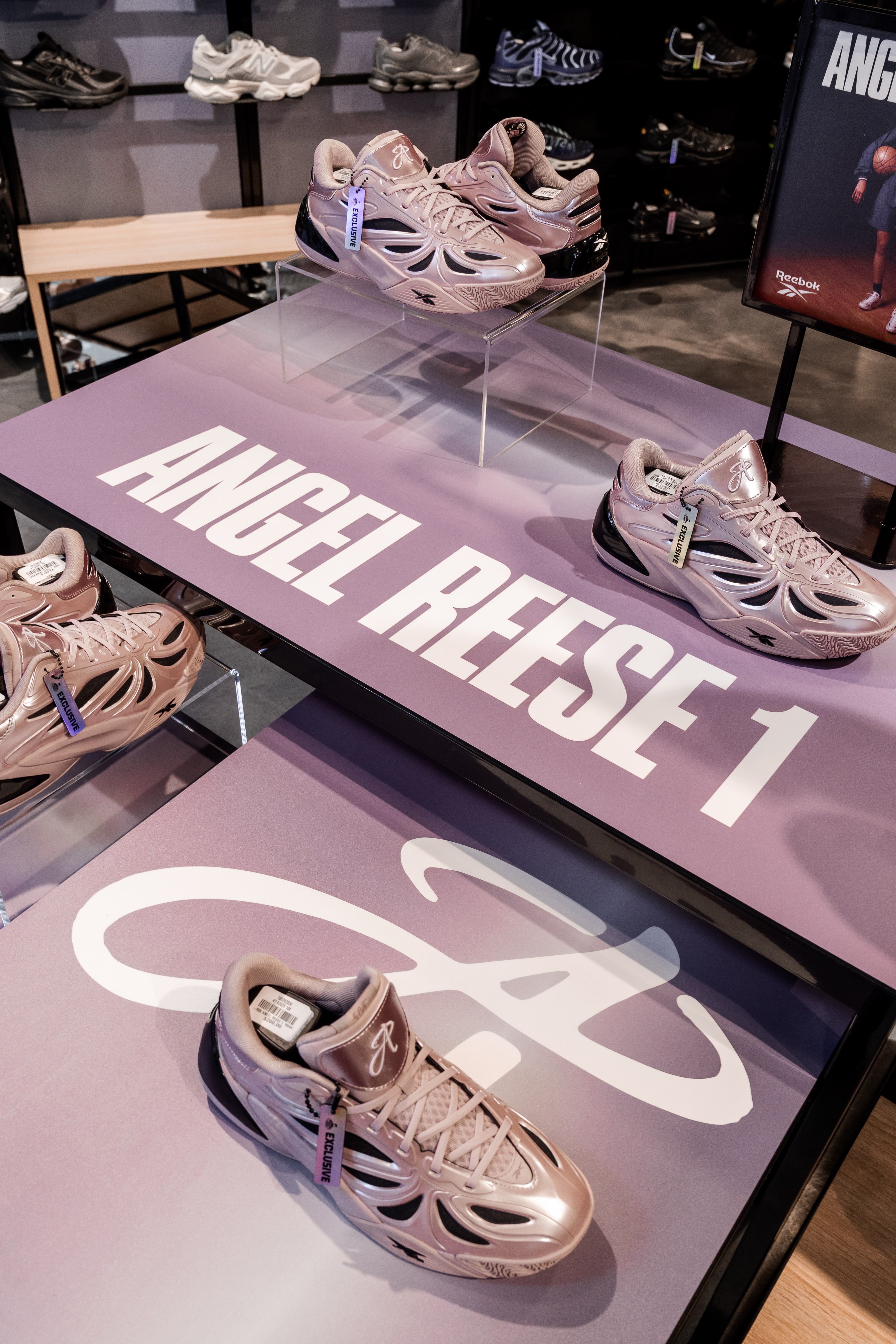 Metallic pink Angel Reese 1 sneakers displayed on lilac plinths beside bold "ANGEL REESE 1" lettering