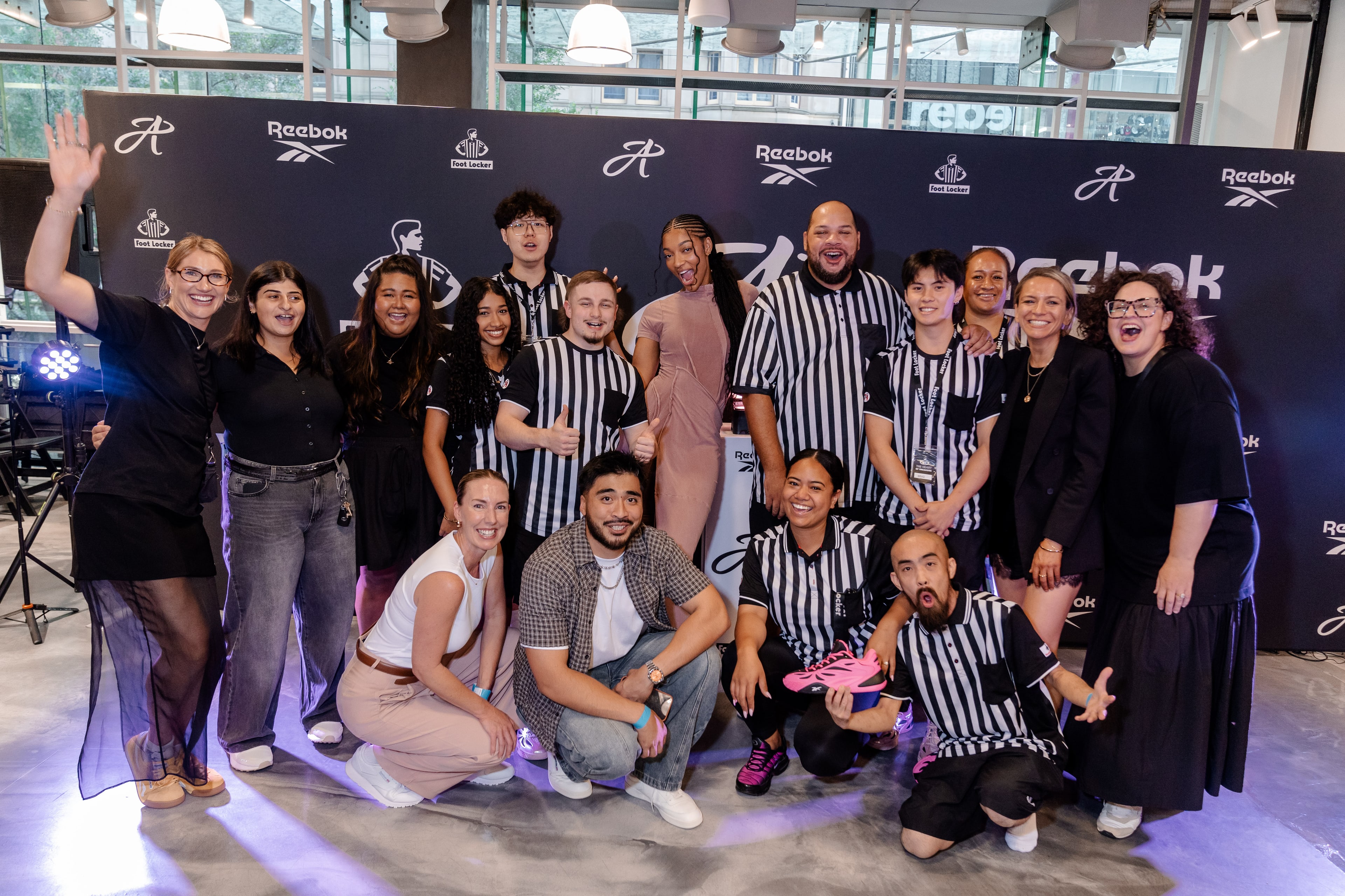 The event team in referee-striped shirts gathered around Angel Reese on the branded media wall