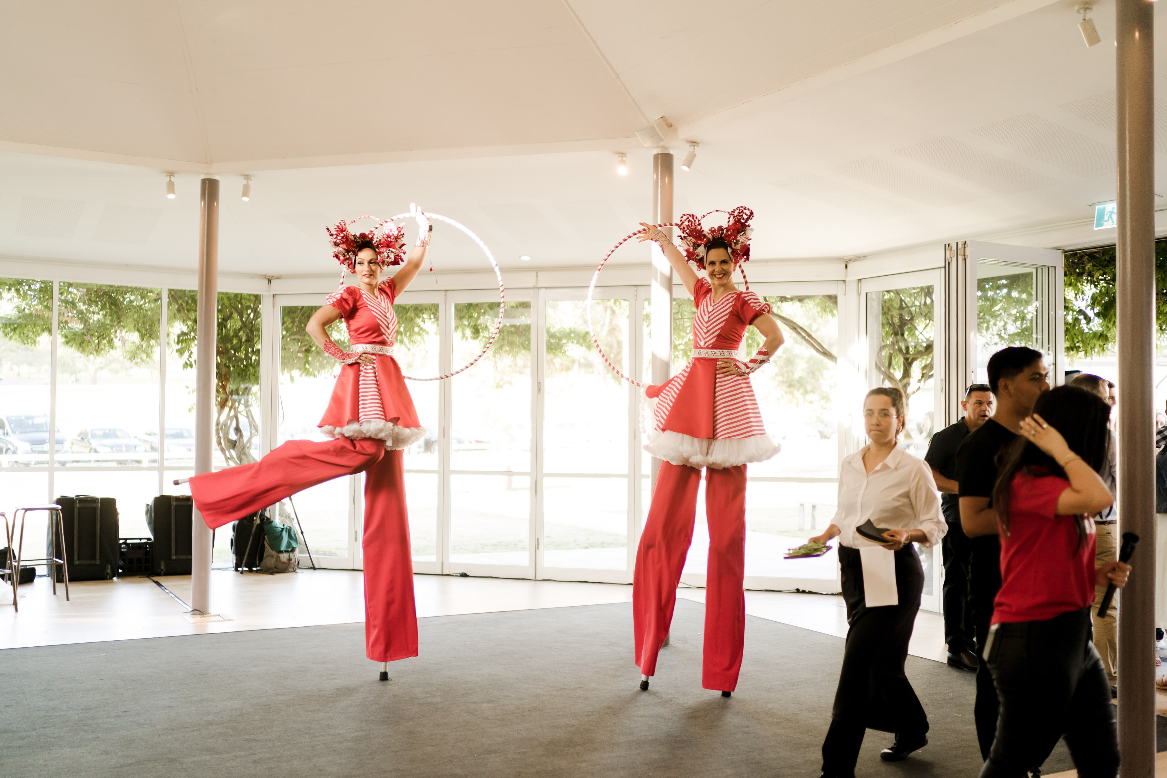 Two red-and-white costumed stilt performers spin hoops inside the marquee as staff and guests look on during the celebration.