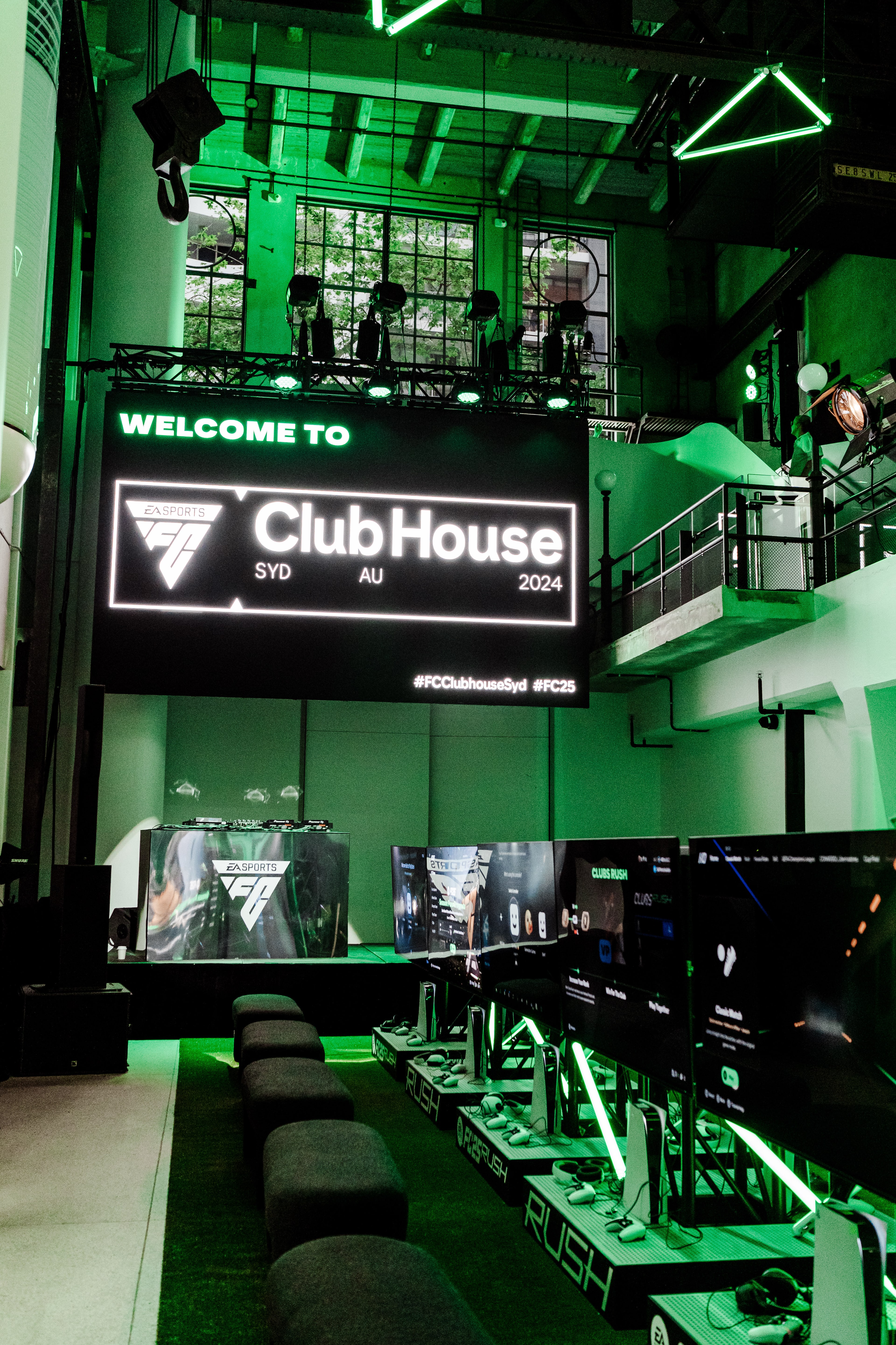 Green-lit industrial hall with a giant 'Welcome to ClubHouse SYD AU 2024' LED screen above rows of gaming stations and neon-trimmed monitors.