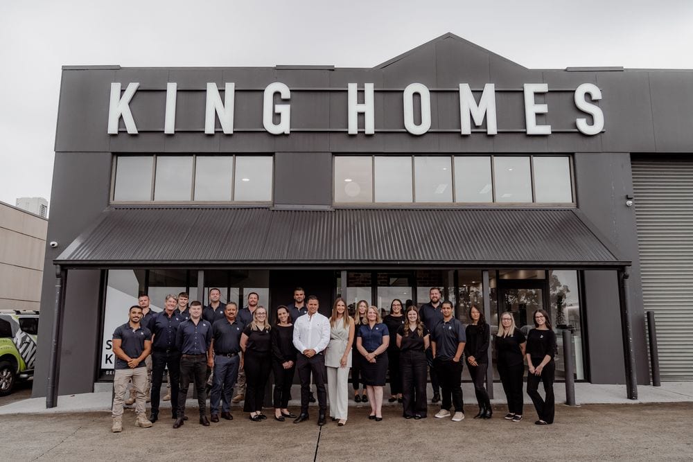 The full King Homes team stands together outside their grey warehouse-style office beneath the large white KING HOMES signage.