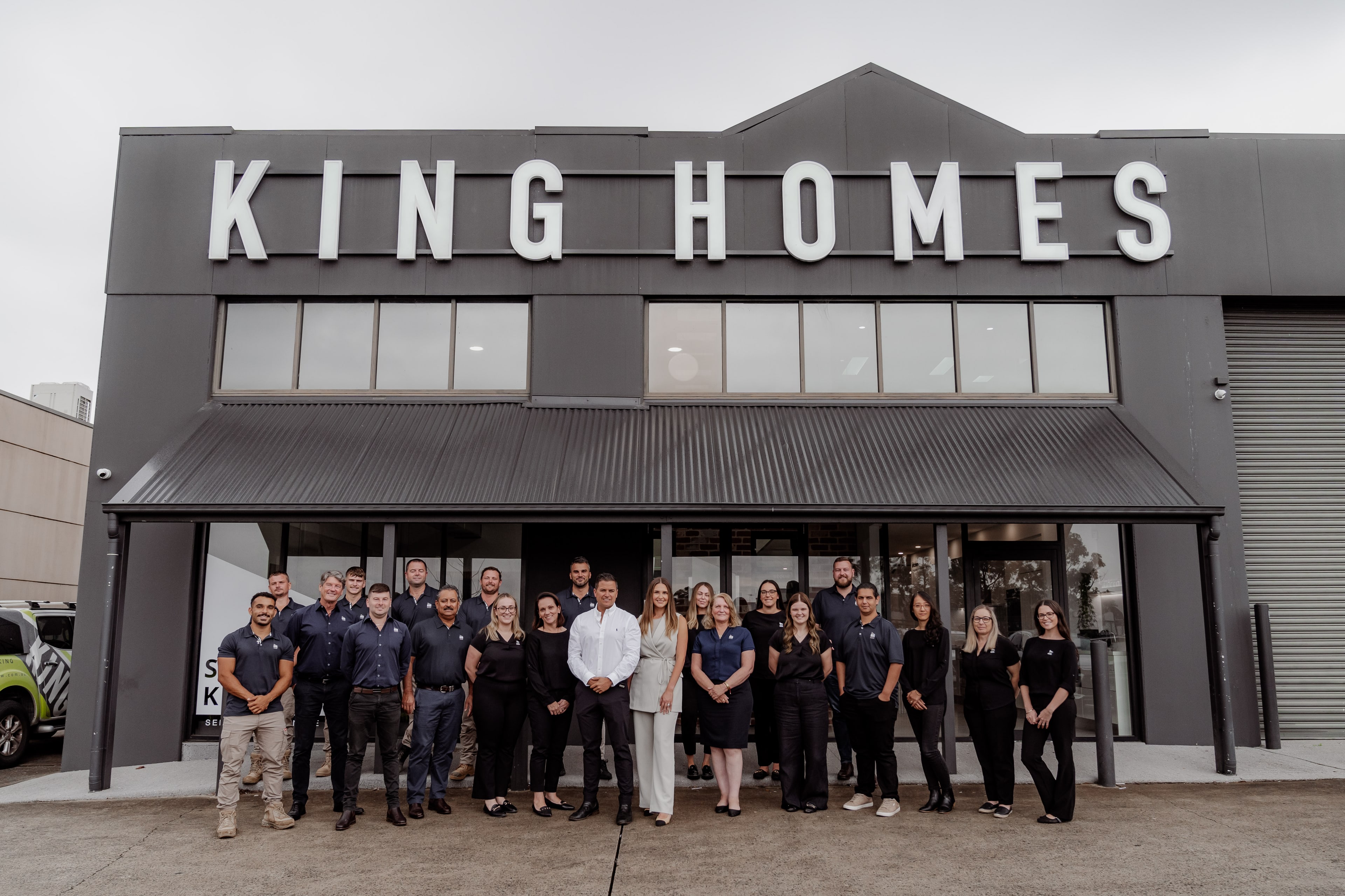 The full King Homes team stands together outside their grey warehouse-style office beneath the large white KING HOMES signage.
