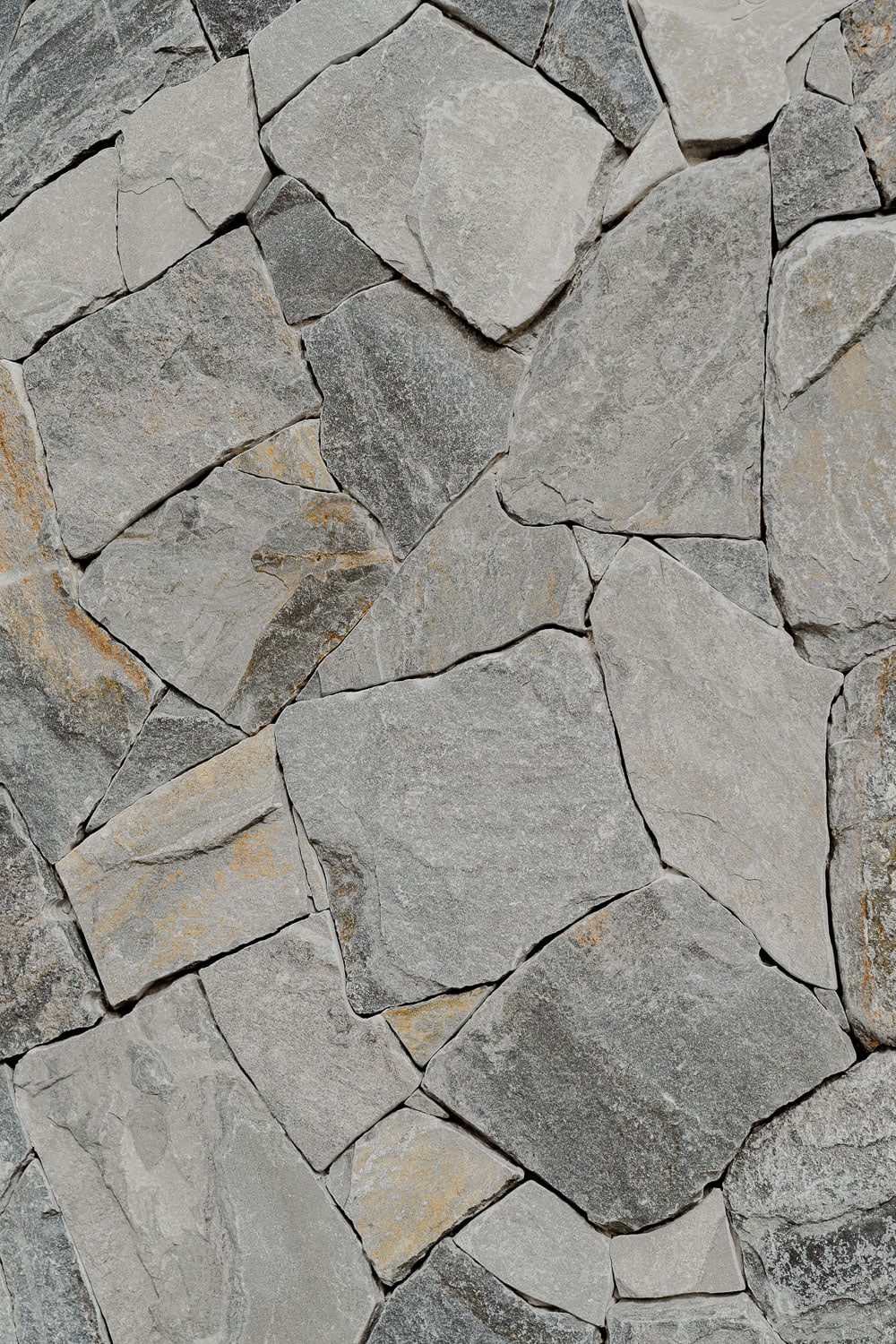 Detail of a dry-stacked natural stone cladding wall showing irregular grey flagstones with warm ochre veining.