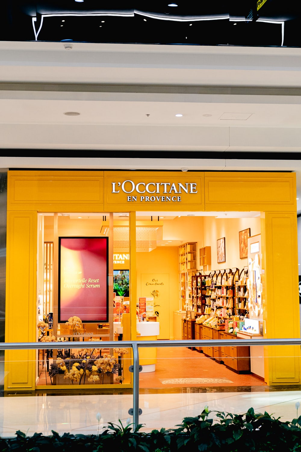 Exterior view of the bright yellow L'Occitane en Provence shopfront, its window display and shelves of products visible from the mall walkway.