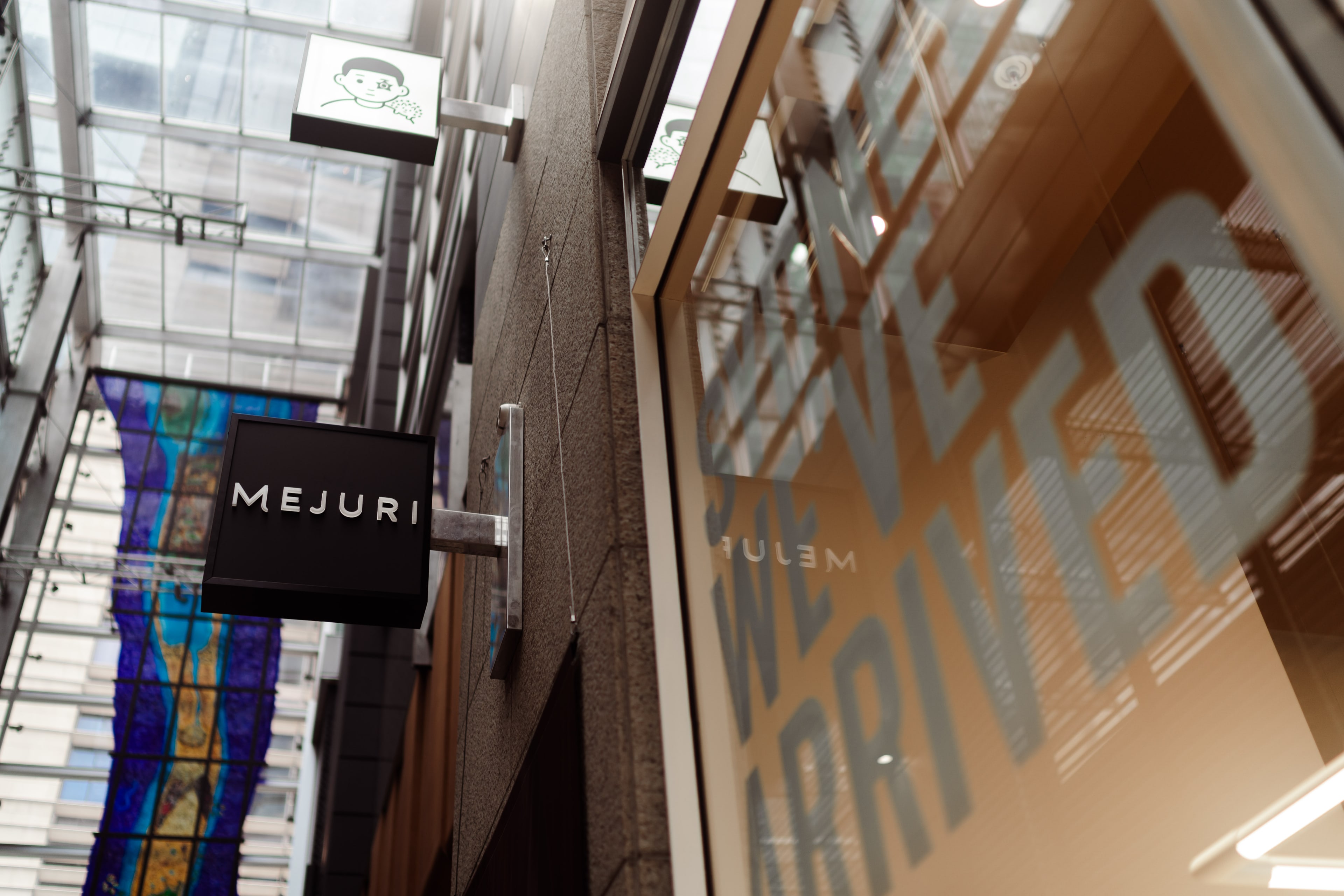 Mejuri storefront sign projecting from a city arcade beside a glass window etched with the words "We've arrived" for the Sydney store launch.