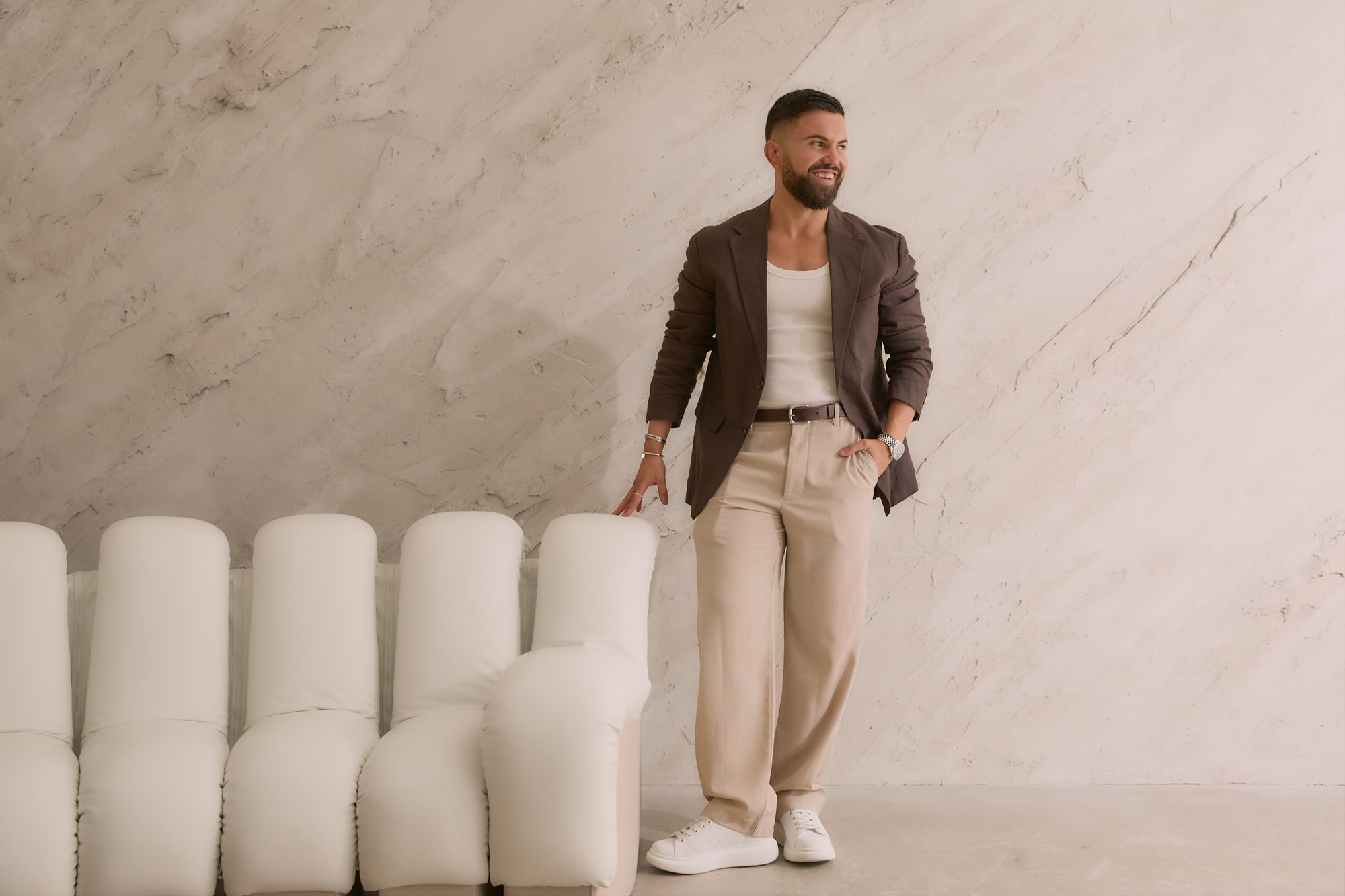 A Peter Petinos Creative team member in a brown blazer standing beside cream studio seating.