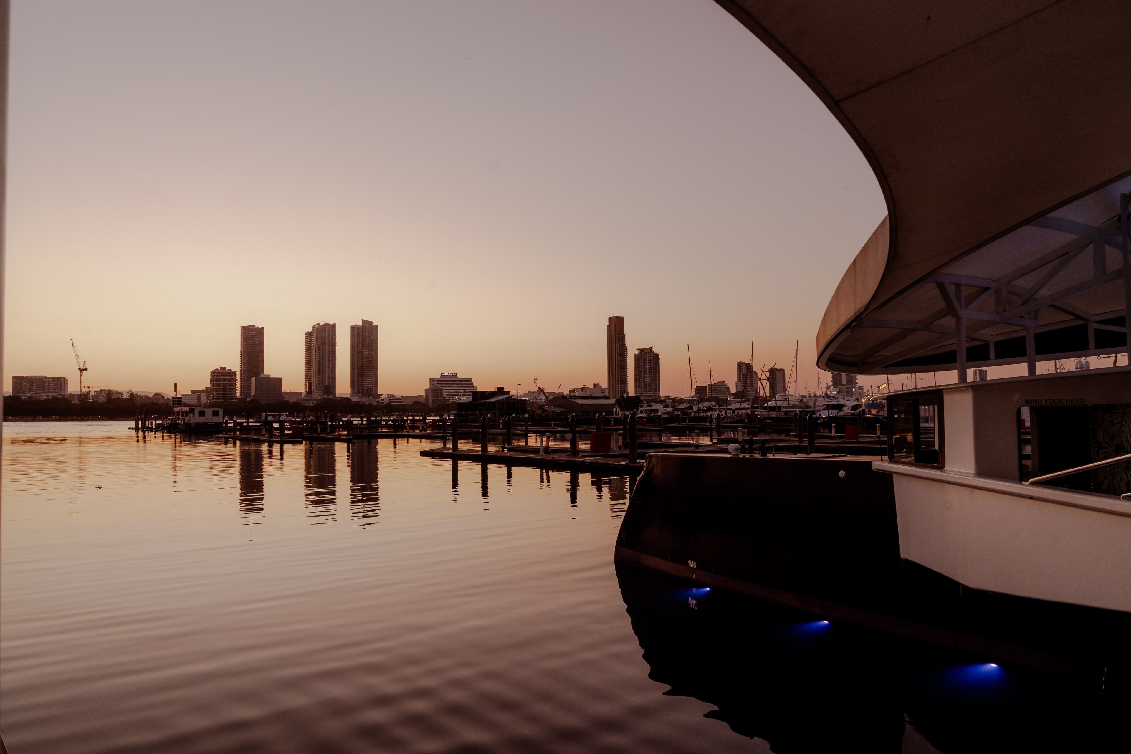 Charter yacht moored at a Gold Coast marina at sunset, with the Southport city skyline reflected across calm water.