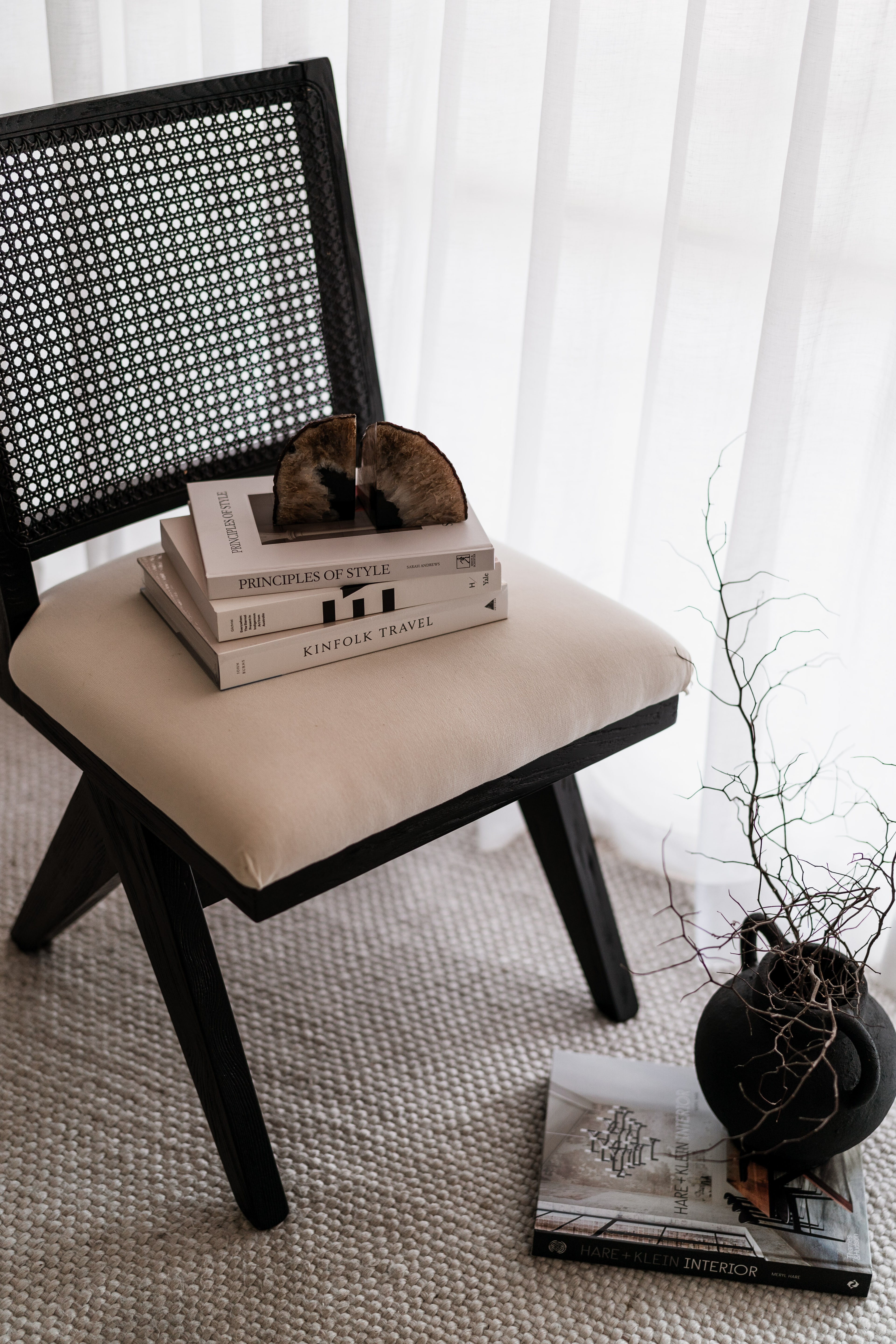 Framed line-art lemon print resting on a black cane chair atop styled coffee-table books, with a twig vase and lemons alongside.