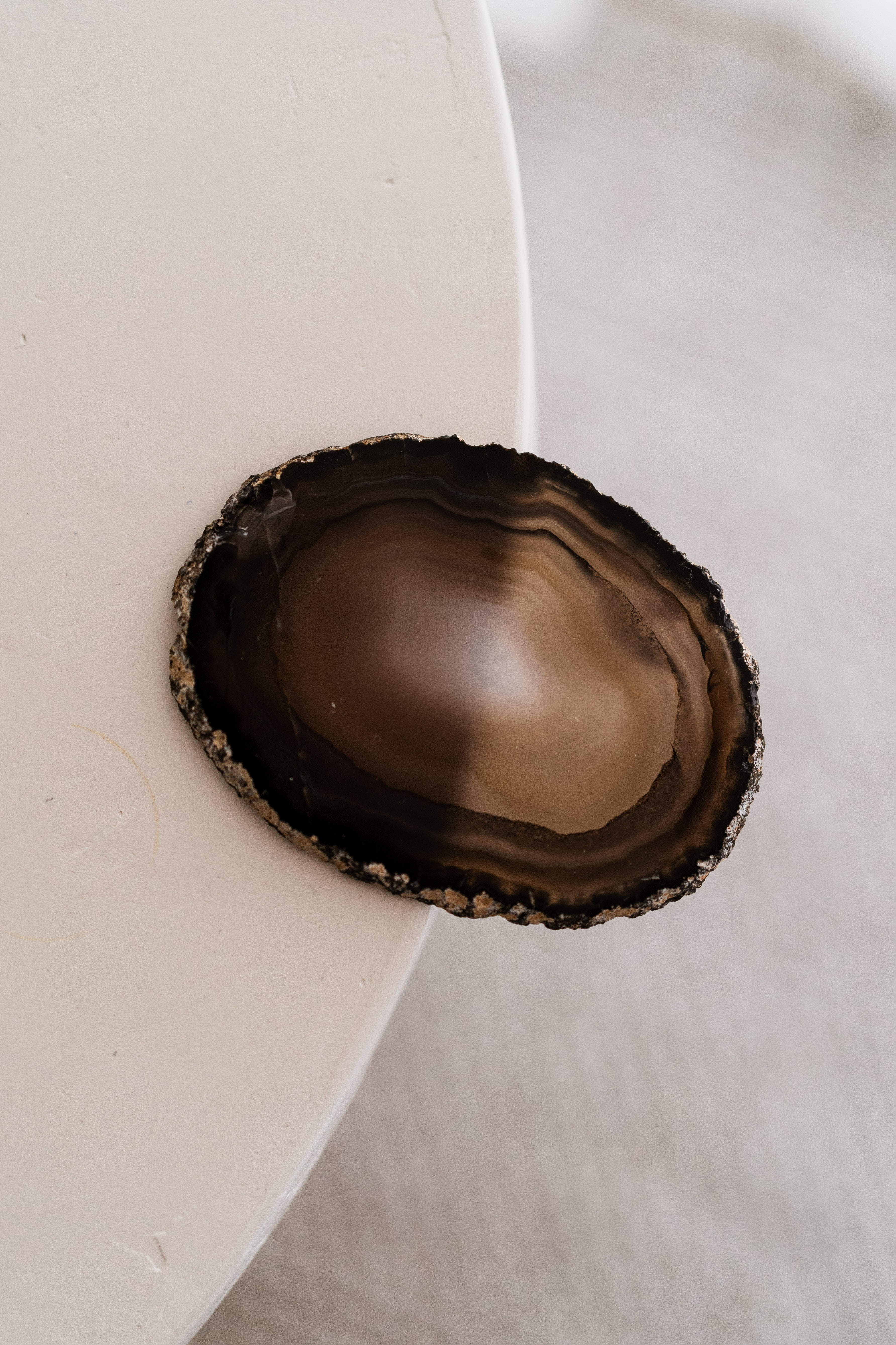 Polished brown agate coaster with a raw crystal edge resting on the rim of a rounded cream side table.