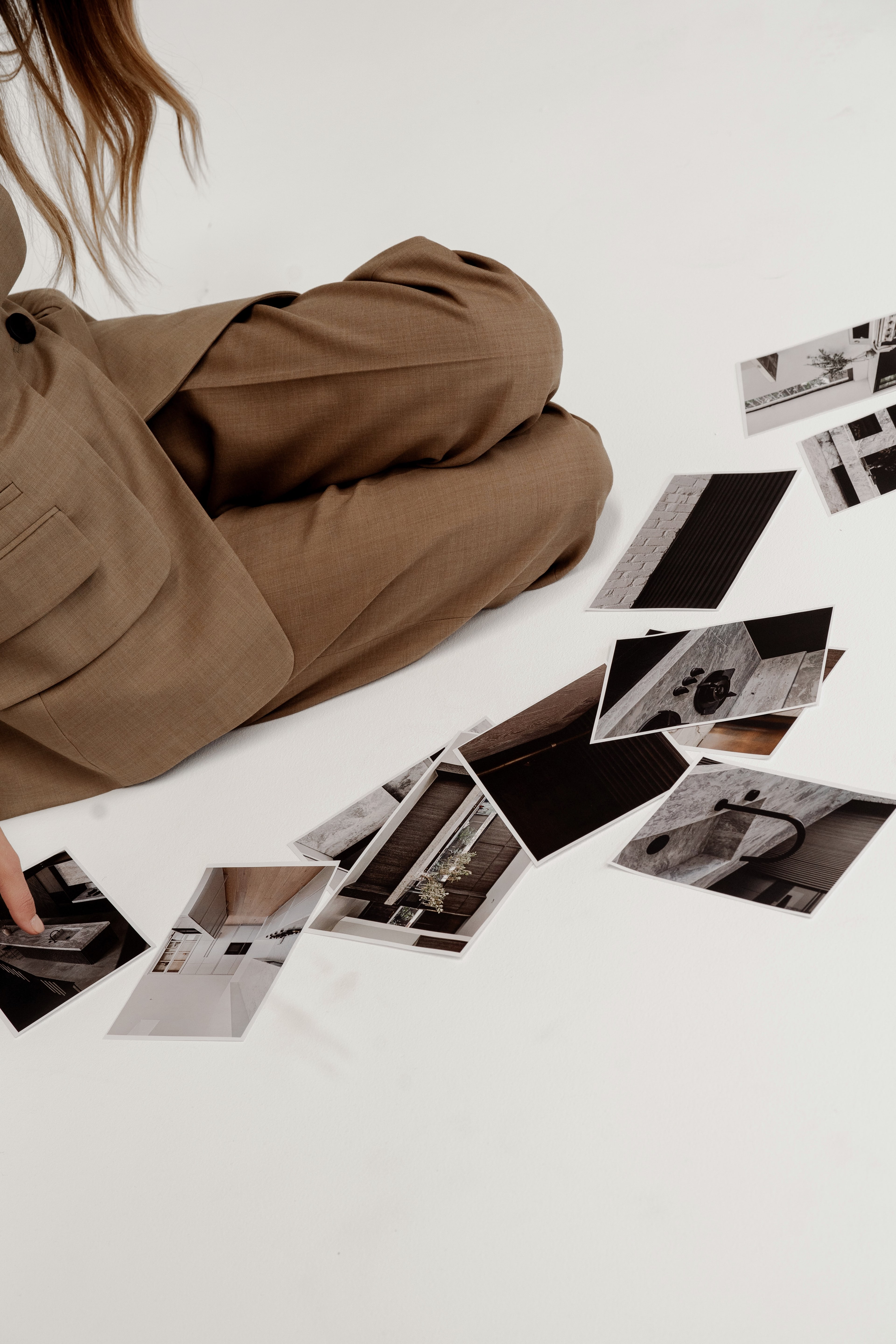 Cropped view of a woman in a brown suit seated on the floor beside scattered black-and-white interior design prints.