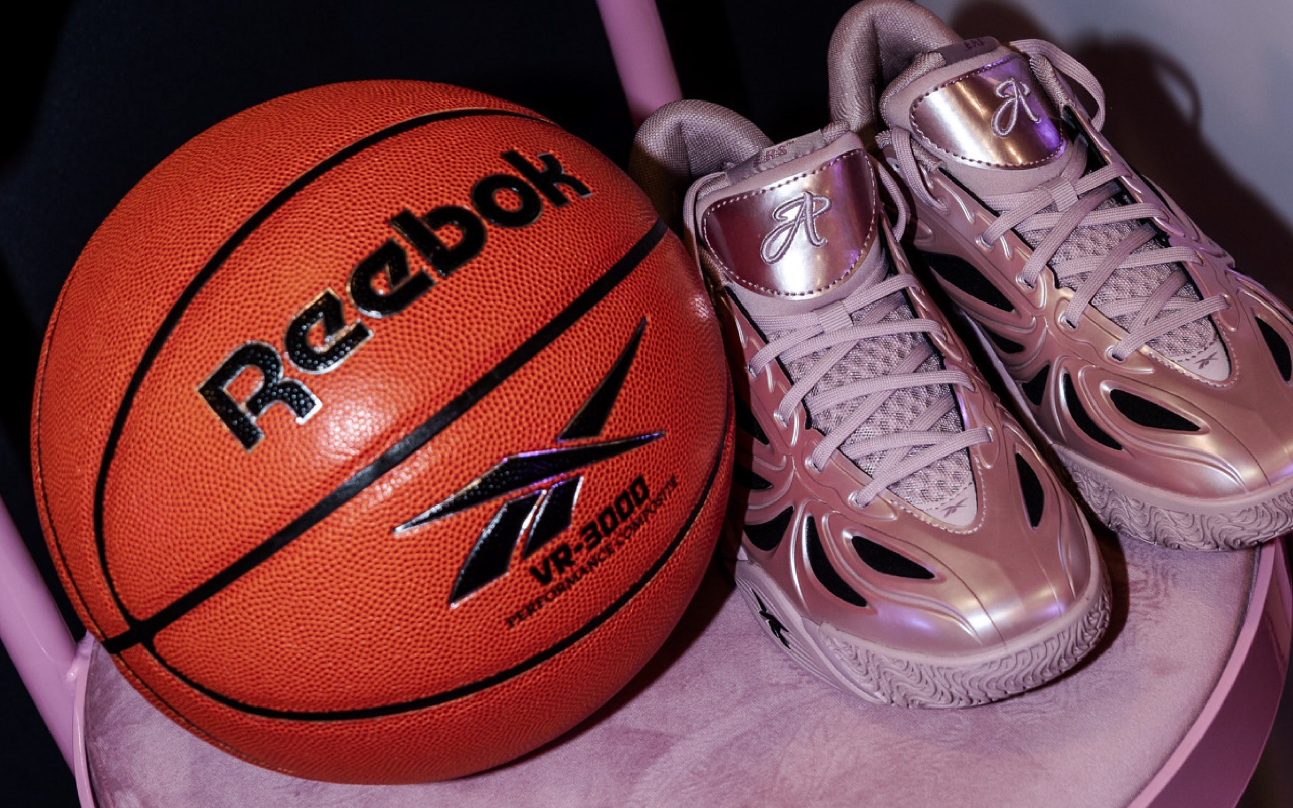Two pink velvet stools holding basketballs flank a plinth displaying the Angel Reese 1 sneaker on a Reebok and Foot Locker backdrop